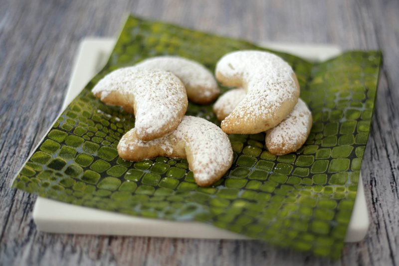 almond crescent cookies on a plate with powdered sugar dusting
