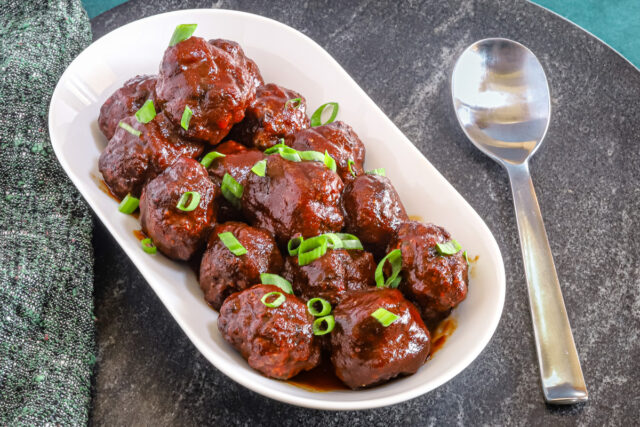 Air fryer meatballs in a serving tray with green onion garnish.