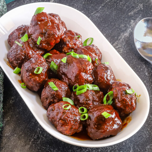Air fryer meatballs in a serving tray with green onion garnish.