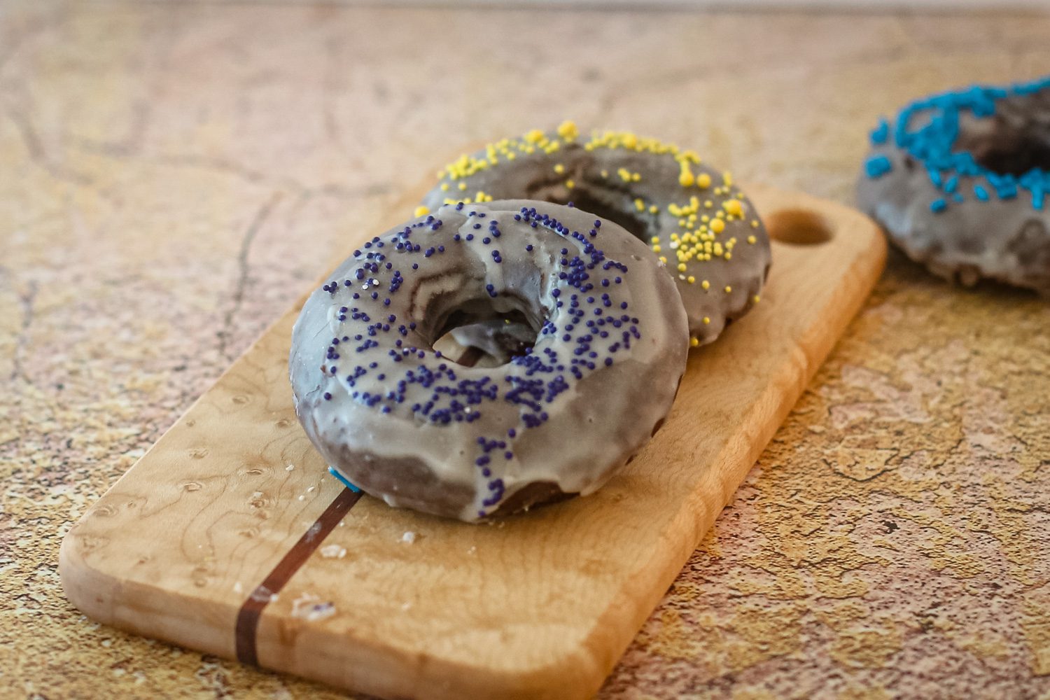 baked chocolate donuts with glaze and sprinkles on a small cutting board