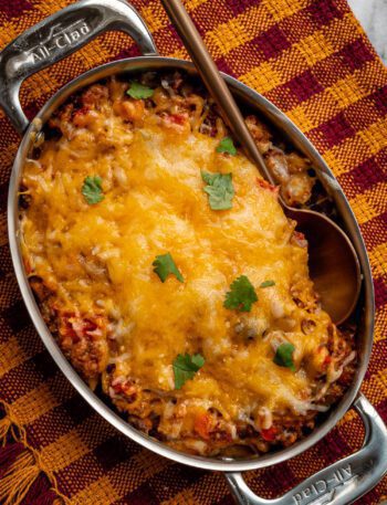 beef and bean taco casserole shown in a pan with melted cheese topping and cilantro leaves
