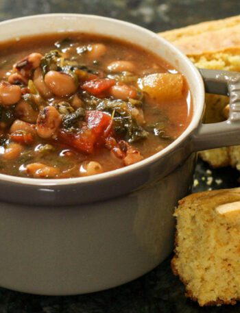 black-eyed pea soup with tomatoes and greens in a small cocotte with cornbread on the side