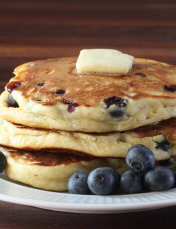 fluffy blueberry pancakes on a plate with butter and fresh blueberries