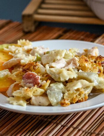 bowtie pasta is shown on a plate with creamy fontina cheese sauce, ham, and sliced tomatoes.