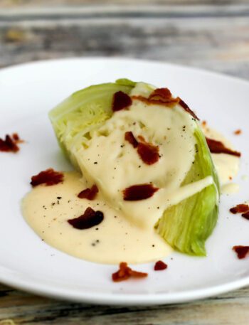 a perfectly cooked wedge of cabbage on a plate with cheese sauce and crumbled bacon