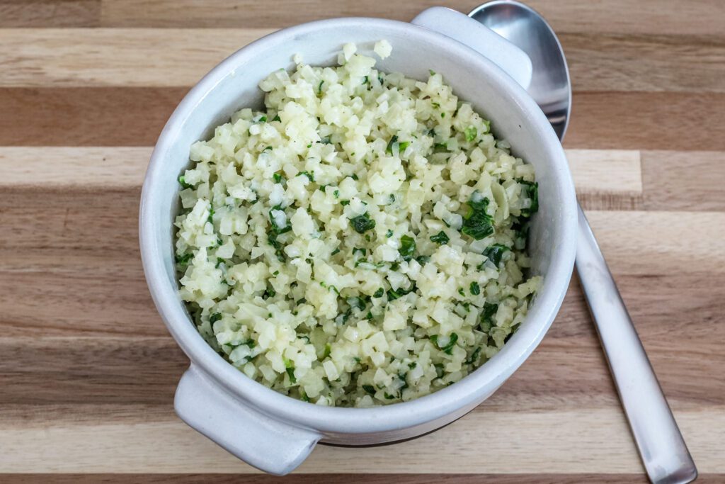 A bowl of cauliflower rice with parsley, Parmesan cheese, and garlic.