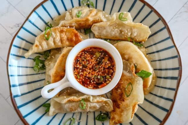 chili crisp sauce in a small bowl in the center of a plate with fried dumplings and garnish of green onions