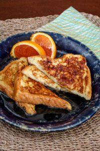 sliced French toast on a plate with orange wedges on the side.