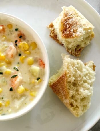 corn and shrimp chowder in a bowl with bread and chives for garnish