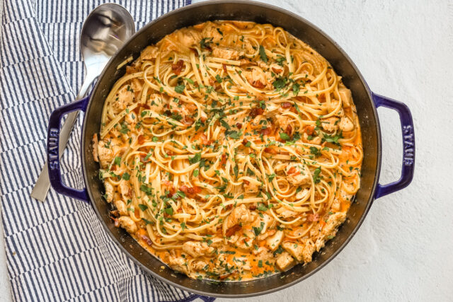 A sauté pan with creamy Cajun seasoned chicken and pasta with crispy pancetta, cream, garlic, and parsley.