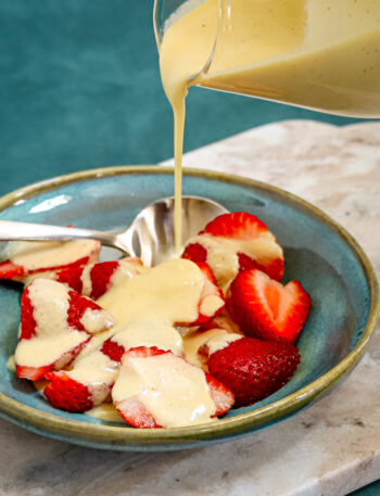 Homemade crème anglaise drizzled over sliced strawberries.