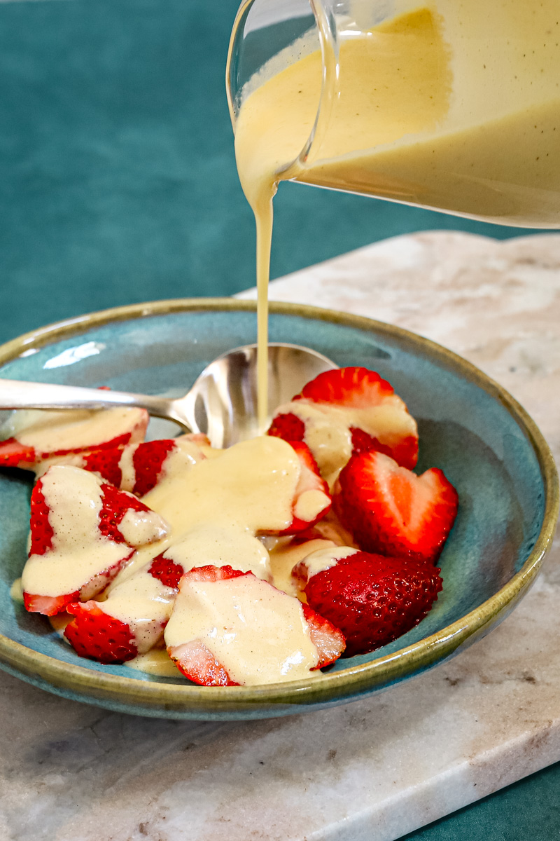 Homemade crème anglaise drizzled over sliced strawberries.