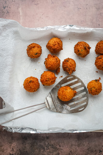 Freshly fried hush puppies from the fryer, draining on paper towels.