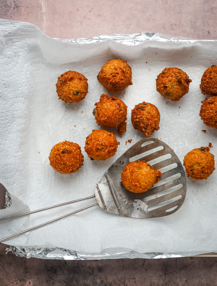 Freshly fried hush puppies from the fryer, draining on paper towels.