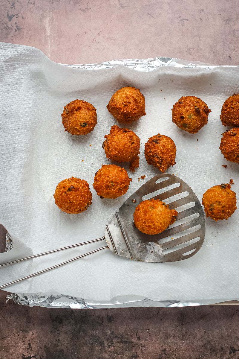 Freshly fried hush puppies from the fryer, draining on paper towels.