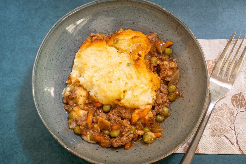 A serving of cottage pie in a bowl with fork on the side