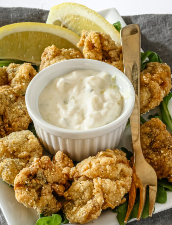 A ramekin with homemade tartar sauce shown with fried oysters.