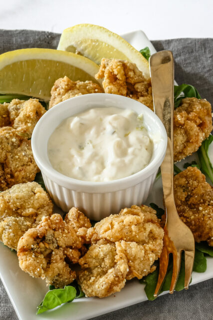 A ramekin with homemade tartar sauce shown with fried oysters.