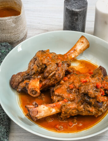 Red wine braised lamb shanks are served with their savory sauce and vegetables.