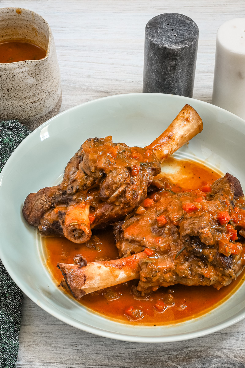 Red wine braised lamb shanks are served with their savory sauce and vegetables.