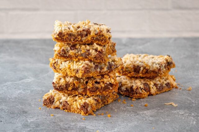 a stack of magic cookie bars with coconut, graham crackers, chocolate chips, and sweetened condensed milk