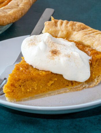 A slice of sweet potato pie on a plate with a dollop of whipped cream and cinnamon sugar.