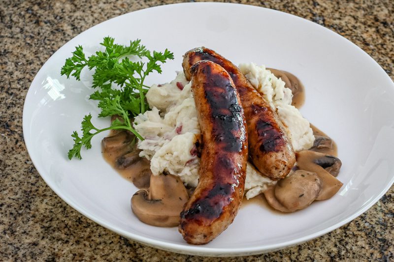 Mushroom sauce with beef stock, garlic, and a splash of beer shown with mashed potatoes and grilled sausages.