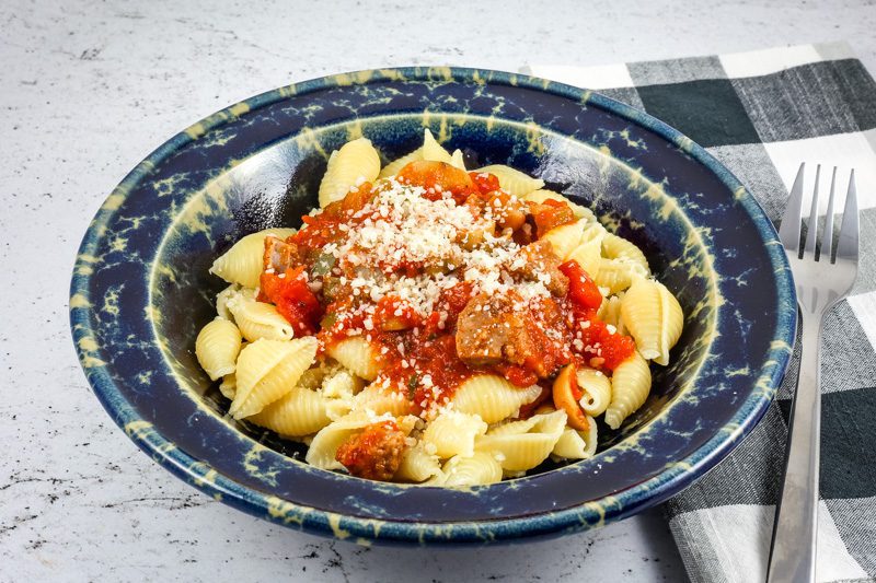 A wide bowl with Neapolitan sauce with sausage and tomatoes over pasta shells.