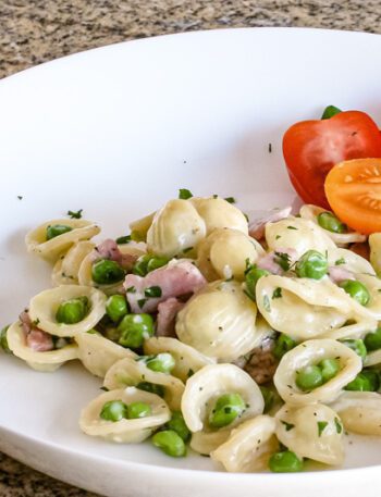 A pasta bowl with a dish of orecchiette with ham, peas, and Parmesan cheese.