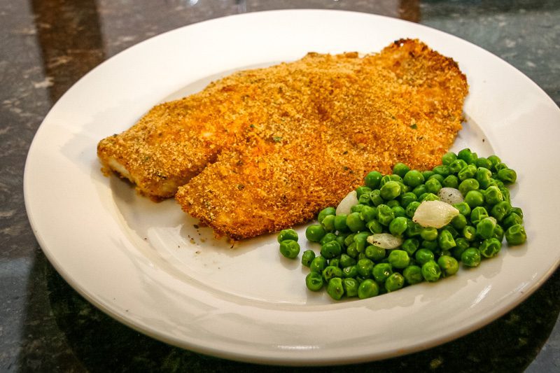 A plate with oven-fried tilapia and peas.