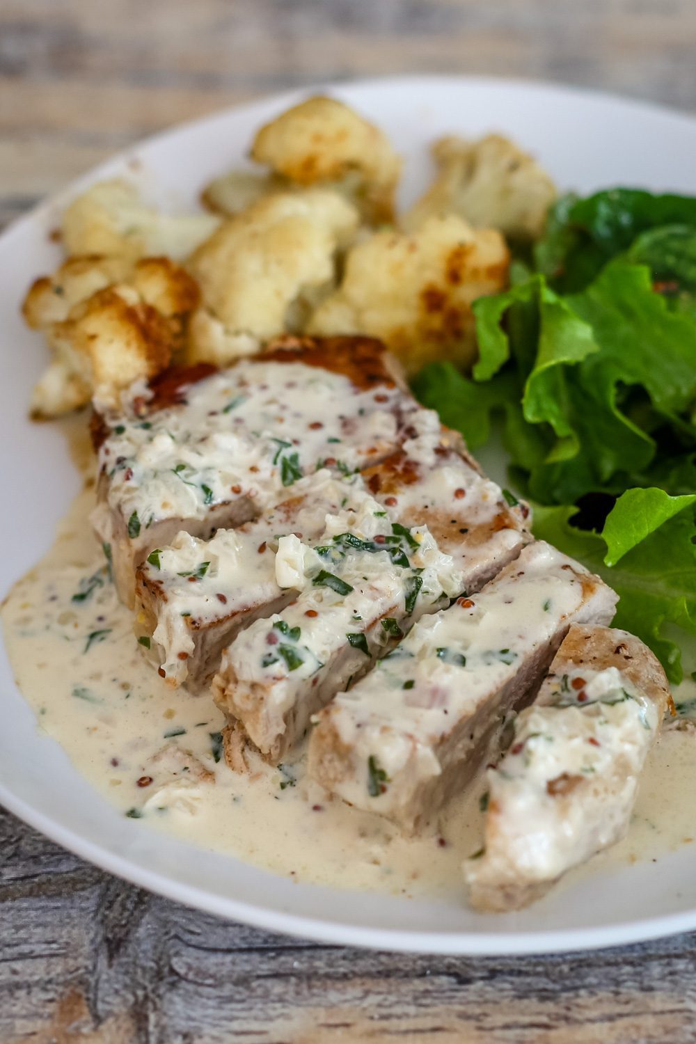 pork chops with mustard cream sauce on a plate with cauliflower and salad