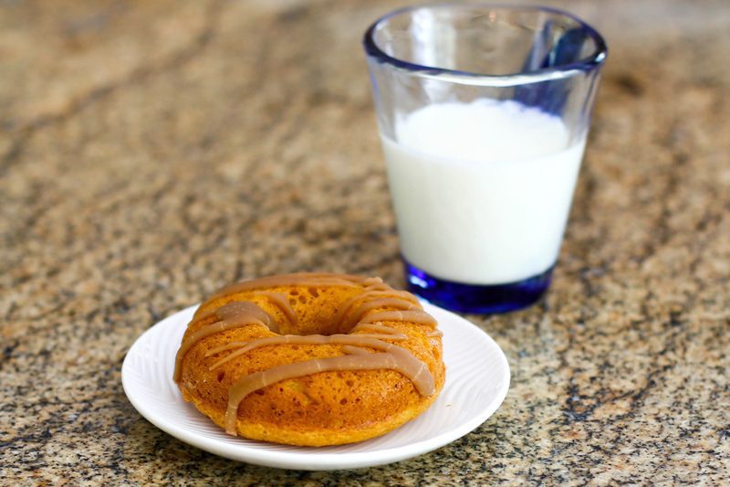 A maple glazed pumpkin donut with a glass of milk.