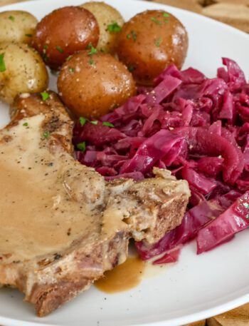 braised red cabbage is shown with a pork chop and baby potatoes on a plate