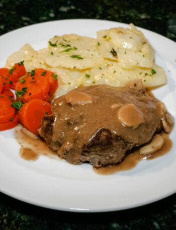 salisbury steaks on a plate with scalloped potatoes and carrots