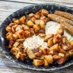 A plate of skillet home fries with sausages and eggs
