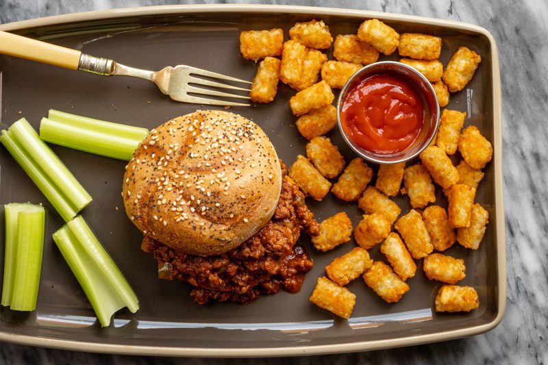 sloppy joe sandwich with tater tots and ketchup on the side.