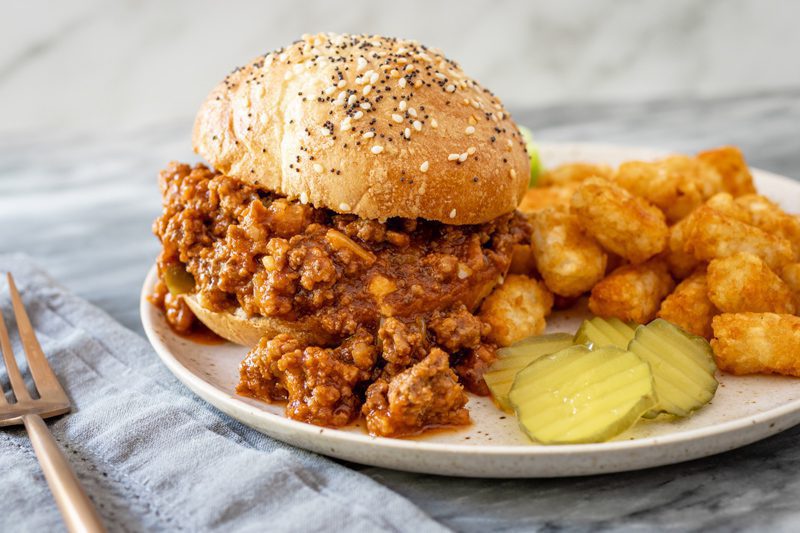 sloppy joe sandwich on a plate with tater tots and pickles