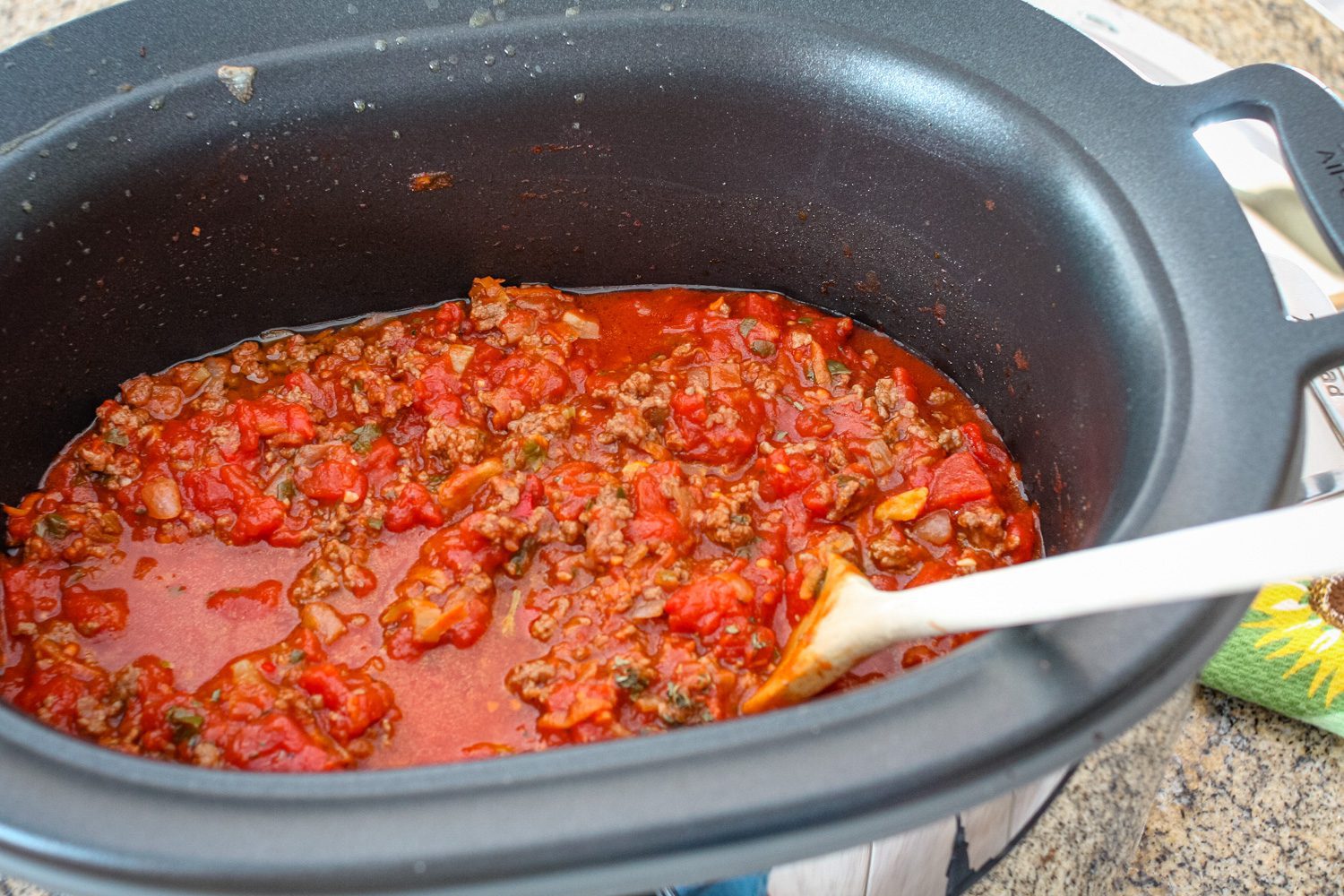 slow cooker bolognese sauce in the slow cooker with a wooden spoon