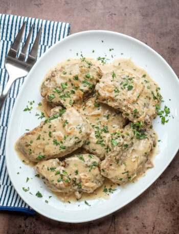 Smothered pork chops on a serving platter with parsley garnish.
