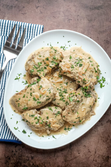Smothered pork chops on a serving platter with parsley garnish.