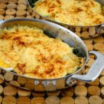 spinach casserole with hard-boiled eggs and cheese sauce in stainless steel gratin dishes