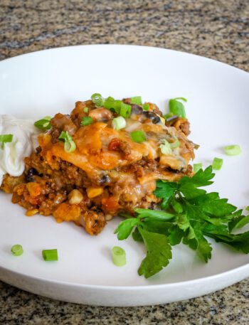layered tamale casserole with ground beef on a plate with herbs, sour cream, and green onions